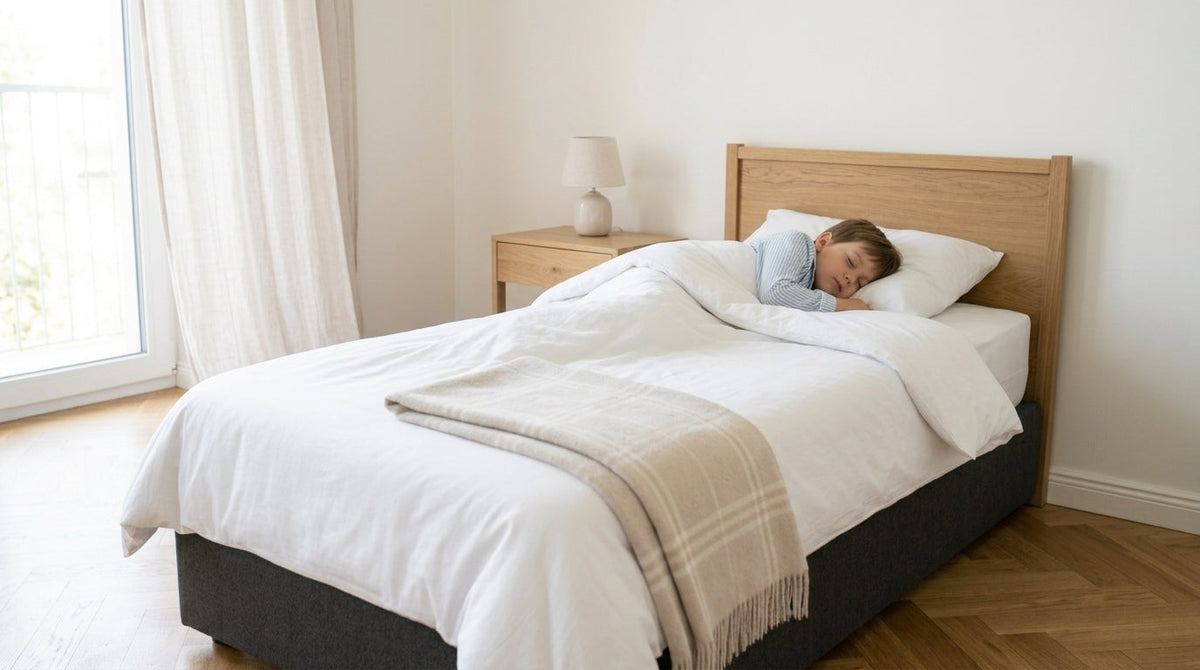 Enfant endormi sous la couette dans un lit au linge blanc, chambre lumineuse